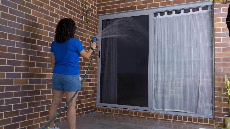 Woman rinsing security screen door with hose