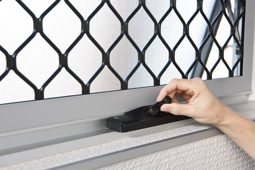 Homeowner adjusting an internal window handle with a diamond security screen in place for airflow and added security.